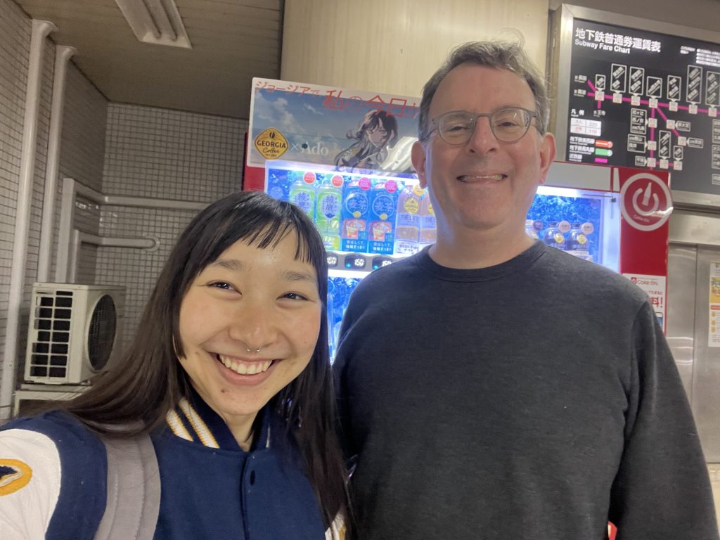 Student Ella Uriu stands next to Professor David Del Testa in a Japanese subway station
