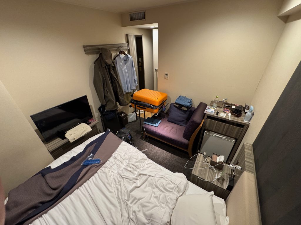 A small hotel room with a bed, desk, TV, and bathroom in a small space.