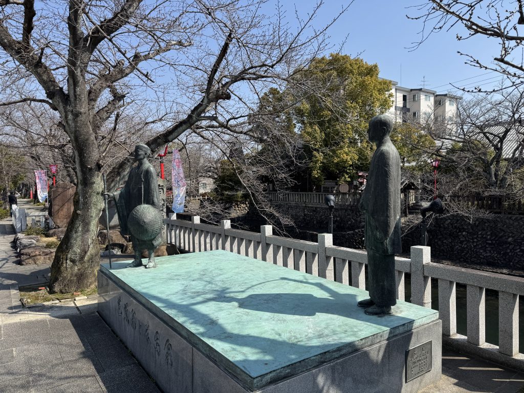 Two bronze statues facing one another on a stone plinth near the Bashō Museum, one of them being a representation of Bashō.