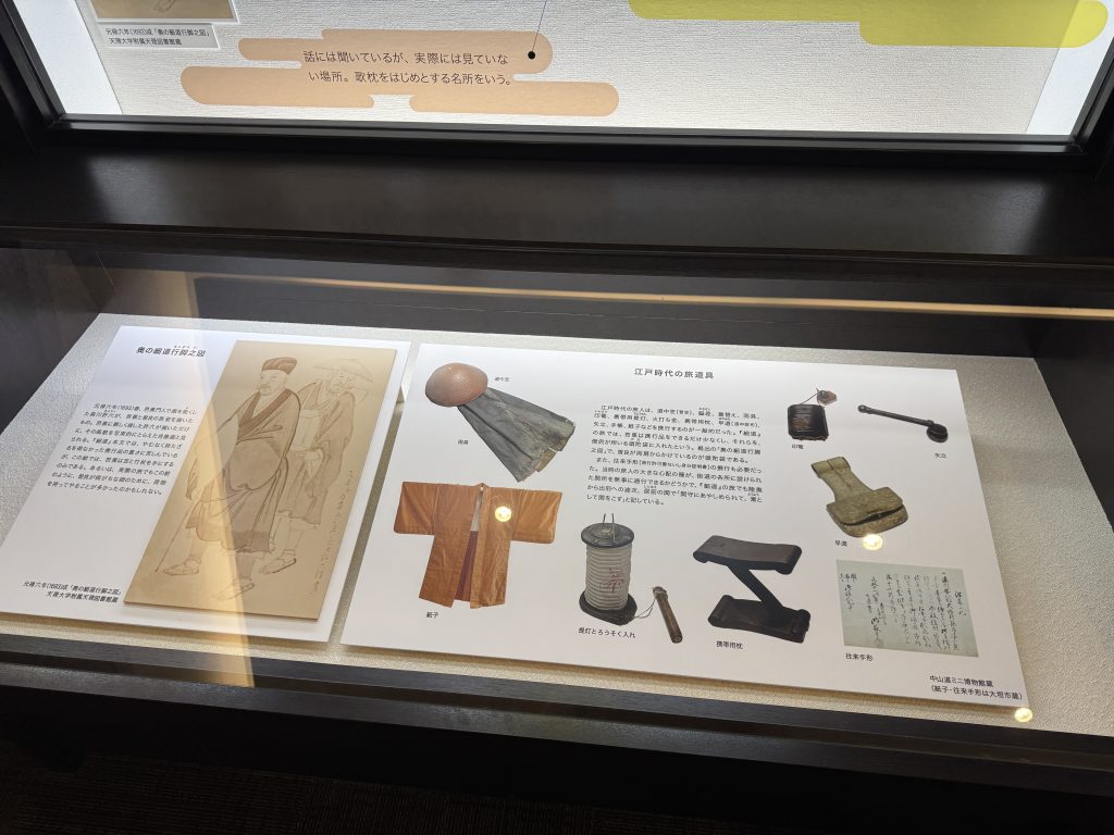 A presentation of the things Bashō took with him on his 1689 journey: a waterproof paper cape, a kimono, a portable lamp, a neck pillow, a writing kit, a pipe, a travel bag, and writing paper.