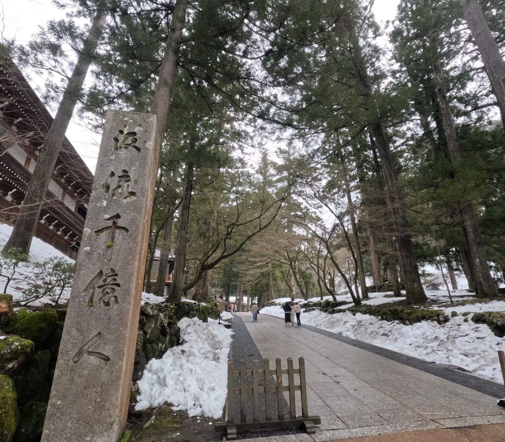Looking on a stone path in trees toward an obscured entrance to teh Daihonzan Eiheiji Temple.