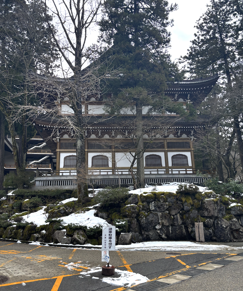 An Eiheiji Temple building surrounded by tall trees, stacked rocks, and moss.